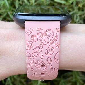May include: A pink silicone watch band with a fall-themed design. The band features a pattern of leaves, acorns, and pumpkins.