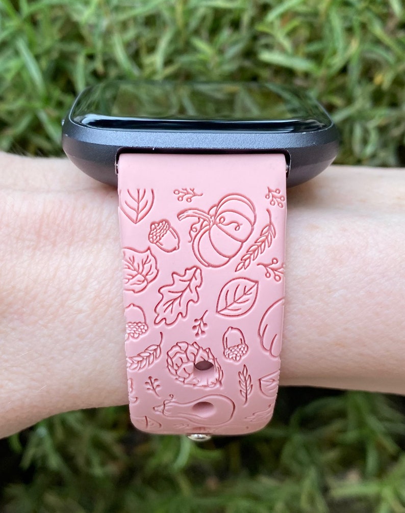 May include: A pink silicone watch band with a fall-themed design. The band features a pattern of leaves, acorns, and pumpkins.