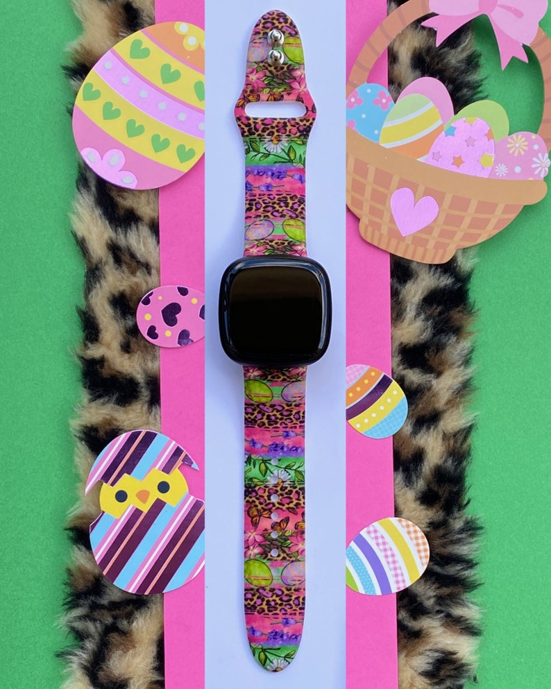 May include: A black smartwatch with a colorful Easter-themed band. The band features a pink, green, and purple floral pattern with leopard print accents. The watch face is black and has a digital display.