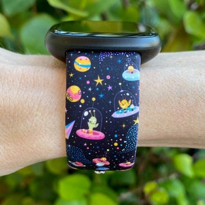 May include: Black watch band with a colorful space-themed print featuring aliens in flying saucers, stars, and planets.