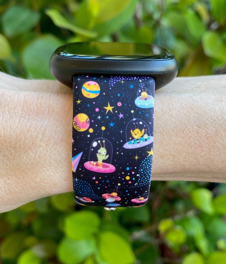 May include: Black watch band with a colorful space-themed print featuring aliens in flying saucers, stars, and planets.