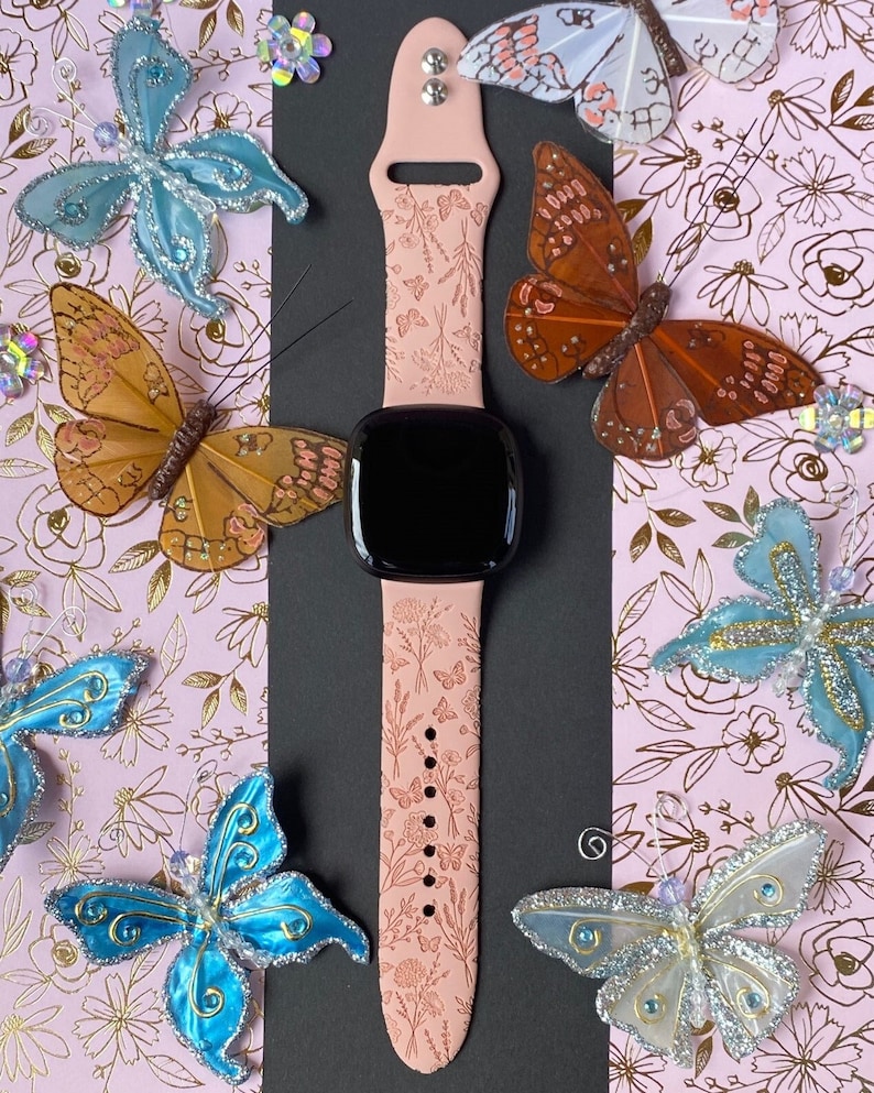 May include: A pink silicone watch band with a floral pattern and a black watch face. The band is surrounded by decorative butterflies in various colors.