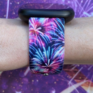 May include: A black smartwatch with a colorful firework print band. The band is made of silicone and has a vibrant design with pink, blue, and purple fireworks.