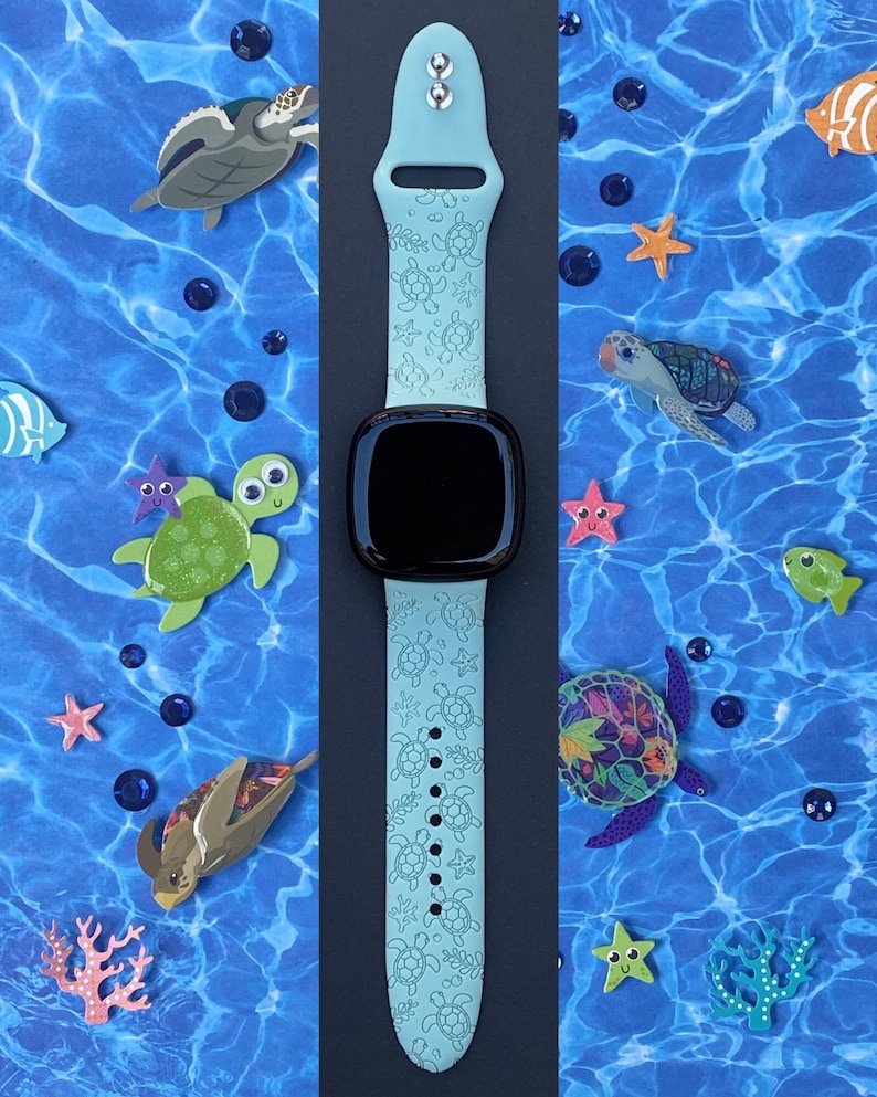 May include: A light blue silicone watch band with a pattern of sea turtles. The band is designed for a smartwatch and has a black watch face.