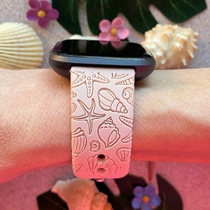K&ouml;nnte beinhalten: Ein rosafarbenes Silikon-Armband mit Muschel- und Seestern-Design. Das Armband ist kompatibel mit einer Smartwatch.