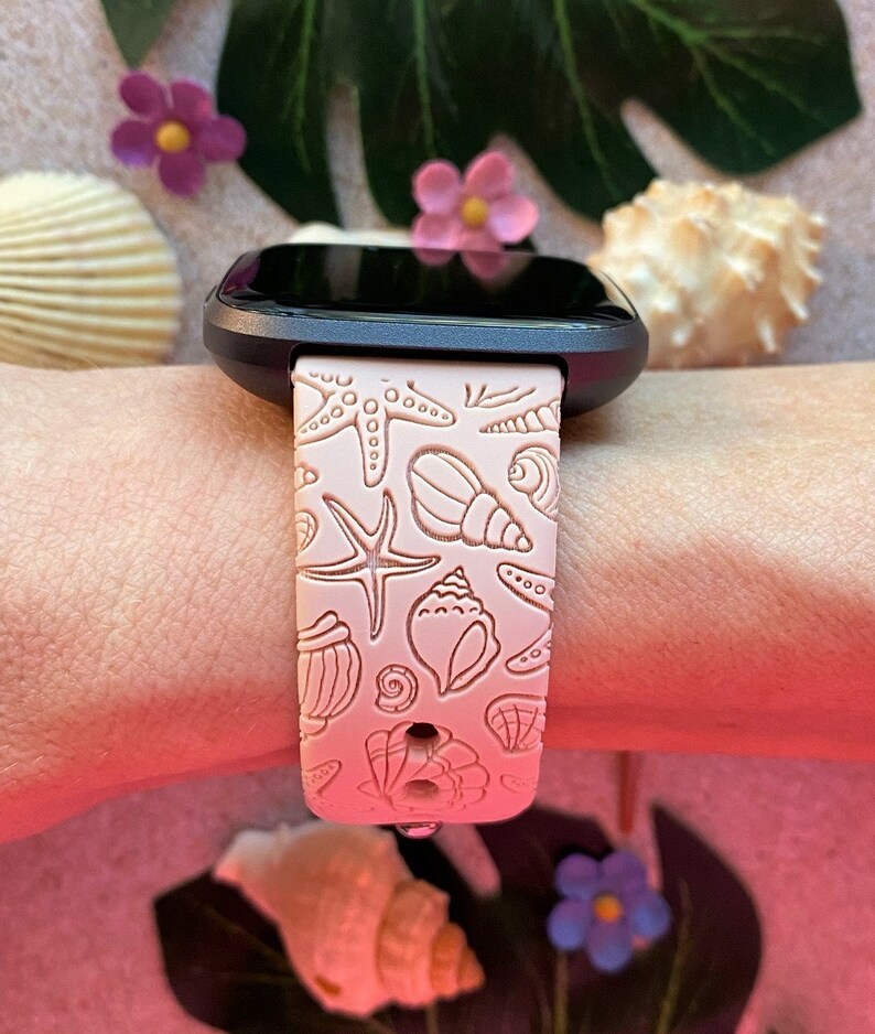 K&ouml;nnte beinhalten: Ein rosafarbenes Silikon-Armband mit Muschel- und Seestern-Design. Das Armband ist kompatibel mit einer Smartwatch.
