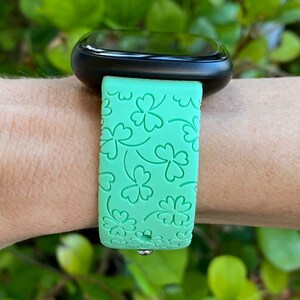 May include: A green smartwatch band with a four-leaf clover pattern.