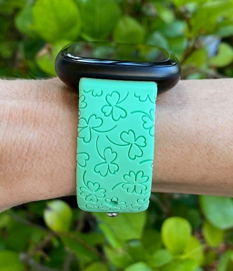 May include: A green smartwatch band with a four-leaf clover pattern.
