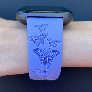 May include: A purple silicone watch band with a black watch face. The band has a repeating pattern of embossed butterflies.
