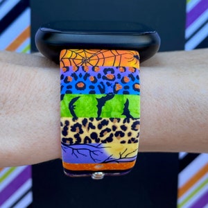 May include: A colorful watch band with a Halloween theme. The band features a spiderweb, bats, leopard print, and a moon with branches. The band is made of silicone and is compatible with most smartwatches.