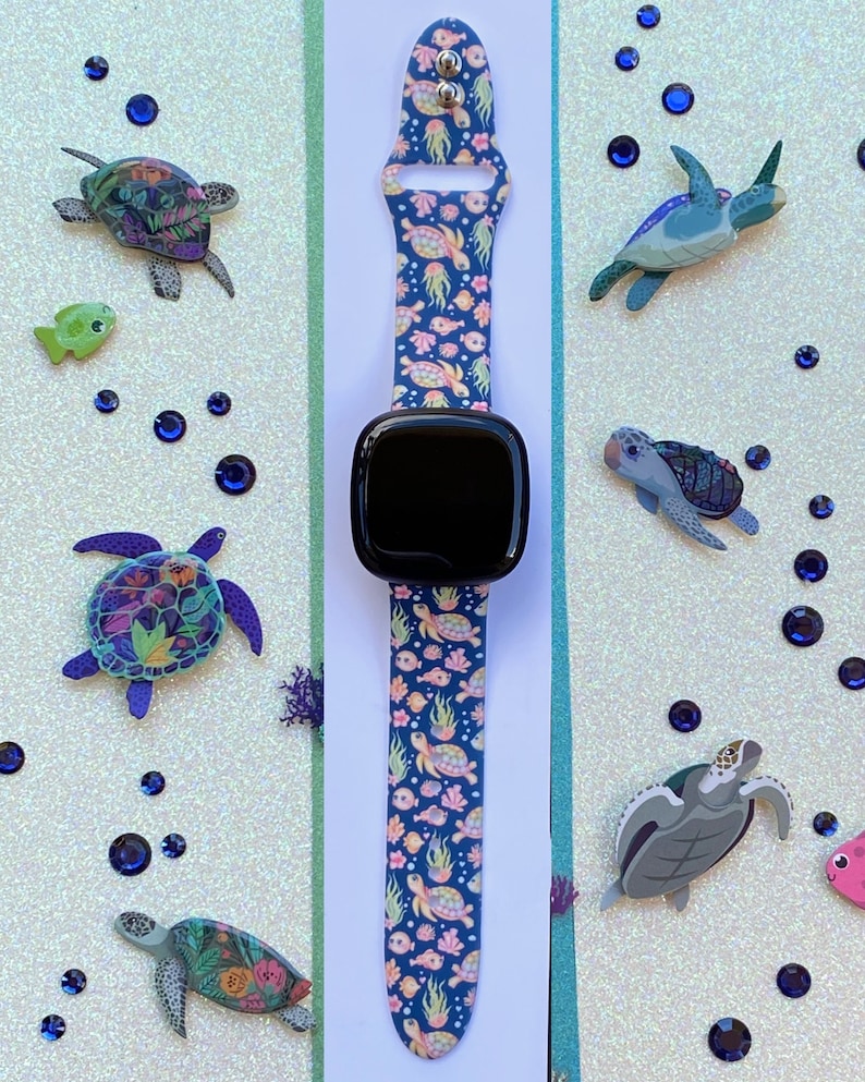 May include: A black smartwatch with a blue and pink patterned band featuring sea turtles, fish, and coral. The band is made of silicone and has a buckle closure.
