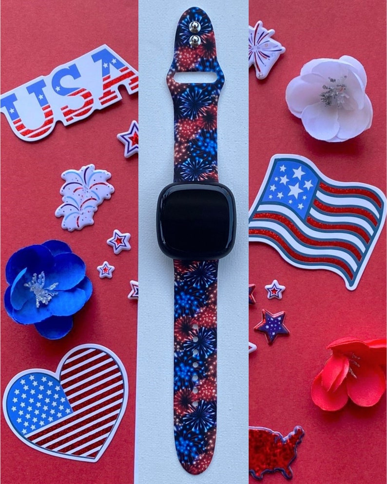 May include: A black smartwatch with a red, white, and blue firework-patterned strap. The image is set against a red background and includes patriotic decorations such as stars, flowers, and a USA flag.