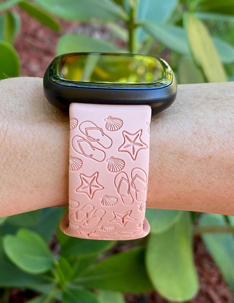 May include: A pink silicone watch band with a beach-themed design. The band features flip flops, seashells, and starfish.
