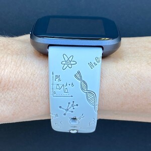 Pode incluir: Um smartwatch cinza com uma pulseira de silicone branca com um design tem&aacute;tico cient&iacute;fico. A pulseira tem uma variedade de s&iacute;mbolos relacionados &agrave; ci&ecirc;ncia, incluindo uma cadeia de DNA, um &aacute;tomo, um b&eacute;quer e um gr&aacute;fico. O texto "H2O" tamb&eacute;m &eacute; vis&iacute;vel na pulseira.