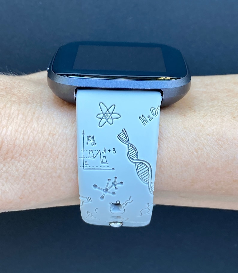Pode incluir: Um smartwatch cinza com uma pulseira de silicone branca com um design tem&aacute;tico cient&iacute;fico. A pulseira tem uma variedade de s&iacute;mbolos relacionados &agrave; ci&ecirc;ncia, incluindo uma cadeia de DNA, um &aacute;tomo, um b&eacute;quer e um gr&aacute;fico. O texto "H2O" tamb&eacute;m &eacute; vis&iacute;vel na pulseira.