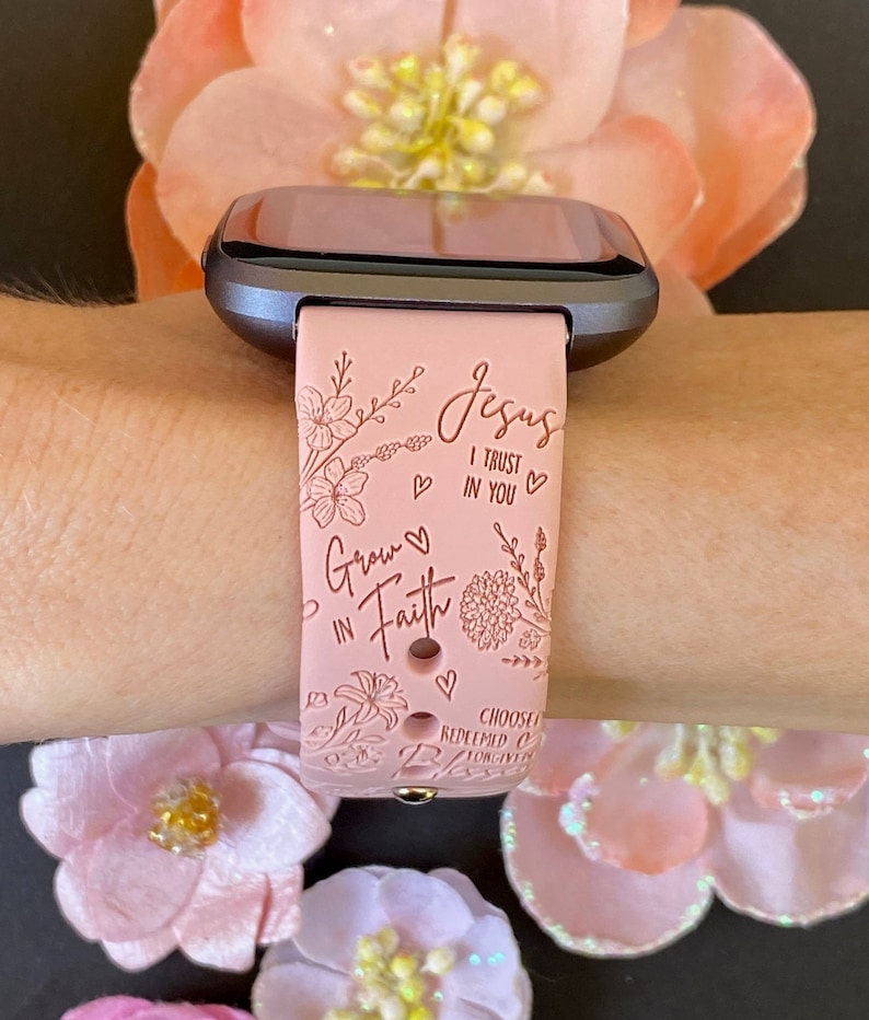 May include: A pink silicone watch band with a floral design and the text "Jesus I trust in you" and "Grow in Faith".