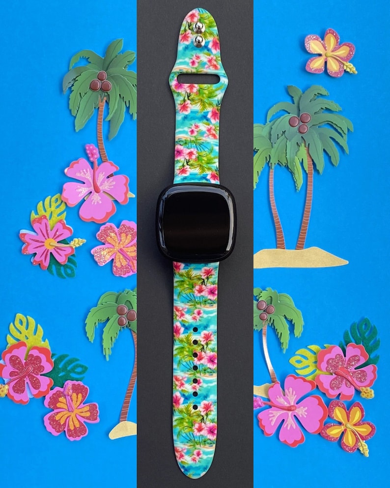 May include: A black smartwatch with a tropical floral print band. The band features pink hibiscus flowers, palm trees, and blue water. The watch face is black and the band is made of silicone.