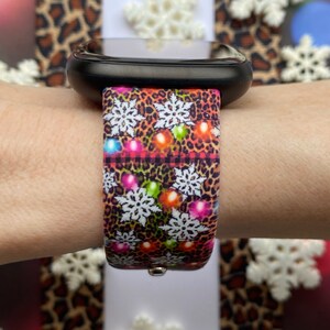 May include: A black smartwatch with a colourful Christmas-themed band. The band features a leopard print pattern with snowflakes and colourful lights.