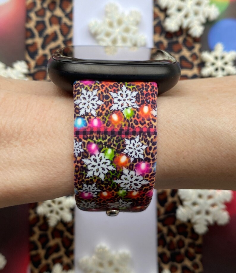 May include: A black smartwatch with a colourful Christmas-themed band. The band features a leopard print pattern with snowflakes and colourful lights.