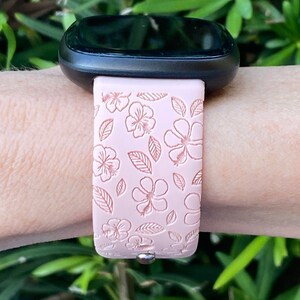 May include: A pink silicone watch band with a floral pattern. The band has a white background with pink flowers and leaves.