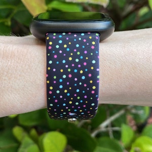 May include: A black smartwatch with a colorful polka dot patterned band. The band has a variety of colors including pink, blue, green, and yellow.
