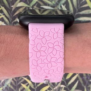 May include: A pink silicone watch band with a floral pattern. The band is designed for a smartwatch and has a silver buckle.