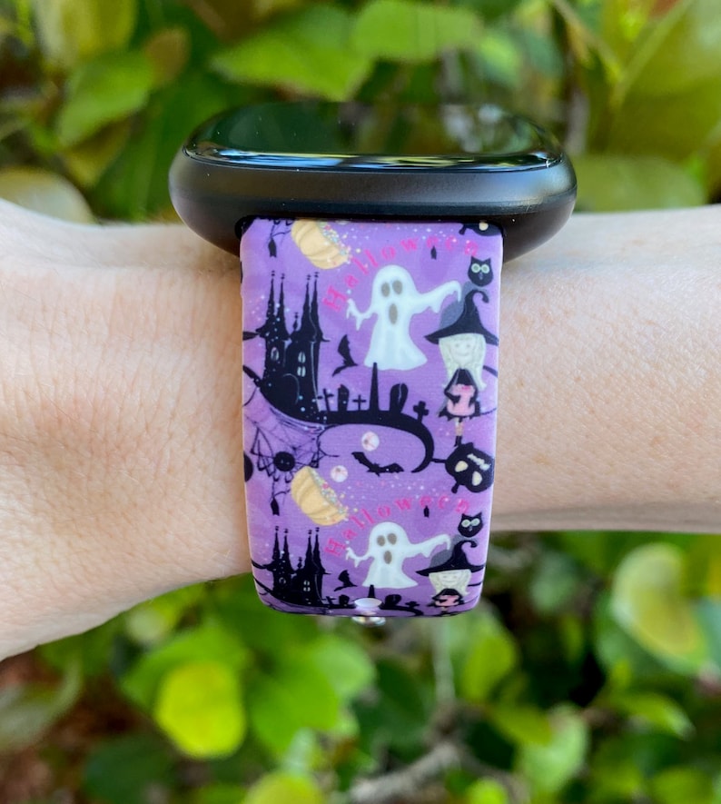 May include: Purple silicone watch band with a Halloween-themed print featuring ghosts, bats, pumpkins, and a castle. The print also includes the word "Halloween" in pink.