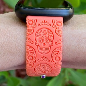 May include: A coral orange silicone watch strap with a sugar skull design. The strap is compatible with smartwatches.