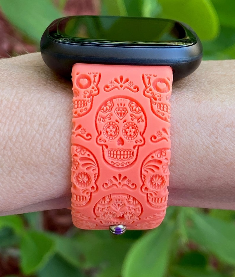 May include: A coral orange silicone watch strap with a sugar skull design. The strap is compatible with smartwatches.