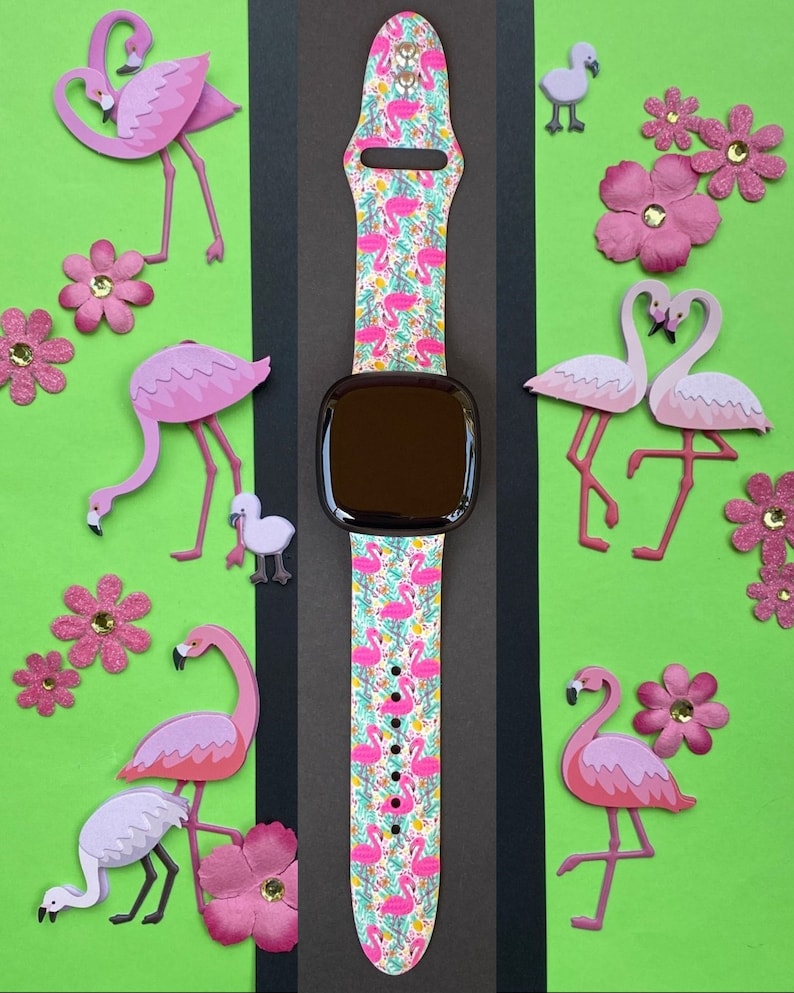 May include: A pink and white Apple Watch band with a flamingo print. The band is shown on a green background with pink flamingo cutouts.