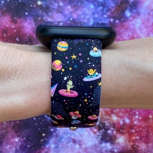 May include: A black smartwatch band with a colorful space-themed design featuring aliens in flying saucers, planets, and stars.