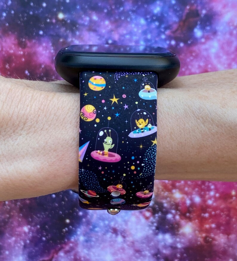 May include: A black smartwatch band with a colorful space-themed design featuring aliens in flying saucers, planets, and stars.
