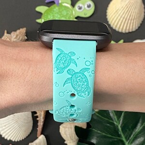 Op de afbeelding: Een turquoise blauwe siliconen horlogeband met een ontwerp van zeeschildpadden en bubbels. De band is compatibel met een smartwatch.