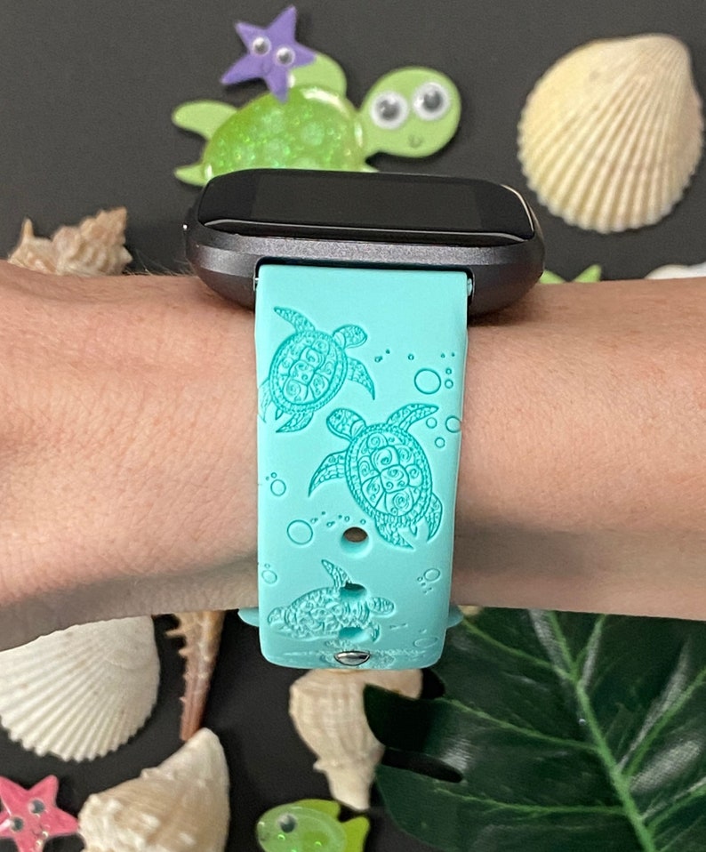 Op de afbeelding: Een turquoise blauwe siliconen horlogeband met een ontwerp van zeeschildpadden en bubbels. De band is compatibel met een smartwatch.
