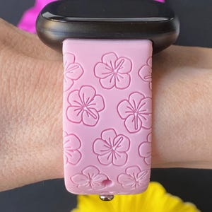 May include: A pink silicone watch strap with a floral pattern. The strap is designed for a smart watch and has a metal clasp.