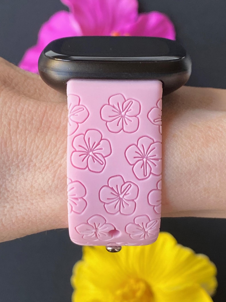 May include: A pink silicone watch strap with a floral pattern. The strap is designed for a smart watch and has a metal clasp.