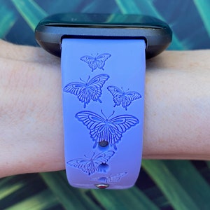 May include: A purple silicone watch band with a butterfly design. The band has five butterflies embossed on it.