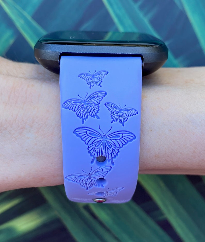 May include: A purple silicone watch band with a butterfly design. The band has five butterflies embossed on it.
