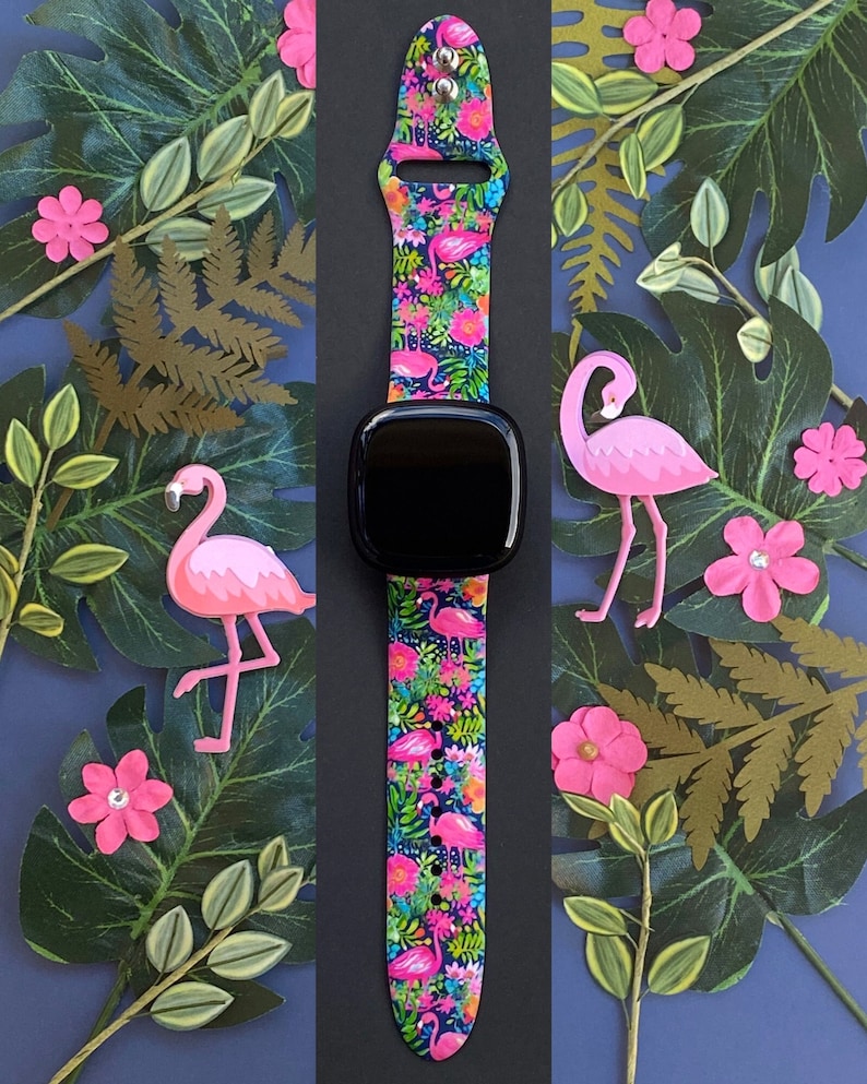 May include: A black smartwatch with a pink and green tropical print watch band featuring pink flamingos and palm leaves.