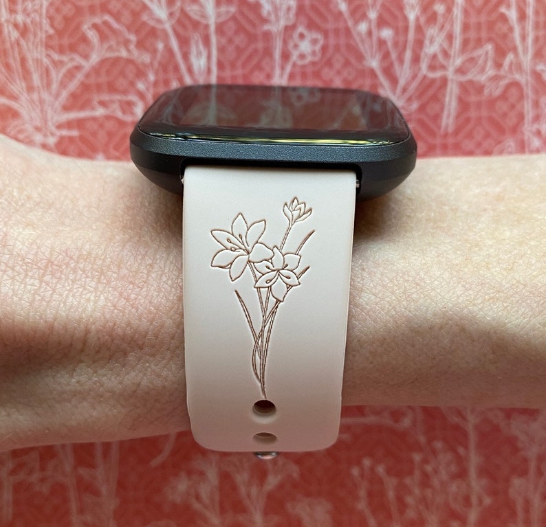 Op de afbeelding: Een wit horlogebandje met een bloemenpatroon. Het bandje is gemaakt van siliconen en heeft een zwart horlogeglas.