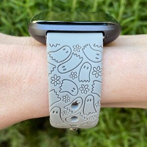 Puede incluir: Una correa de reloj de silicona gris con un patr&oacute;n de fantasmas. La correa est&aacute; dise&ntilde;ada para un reloj inteligente con una esfera negra.