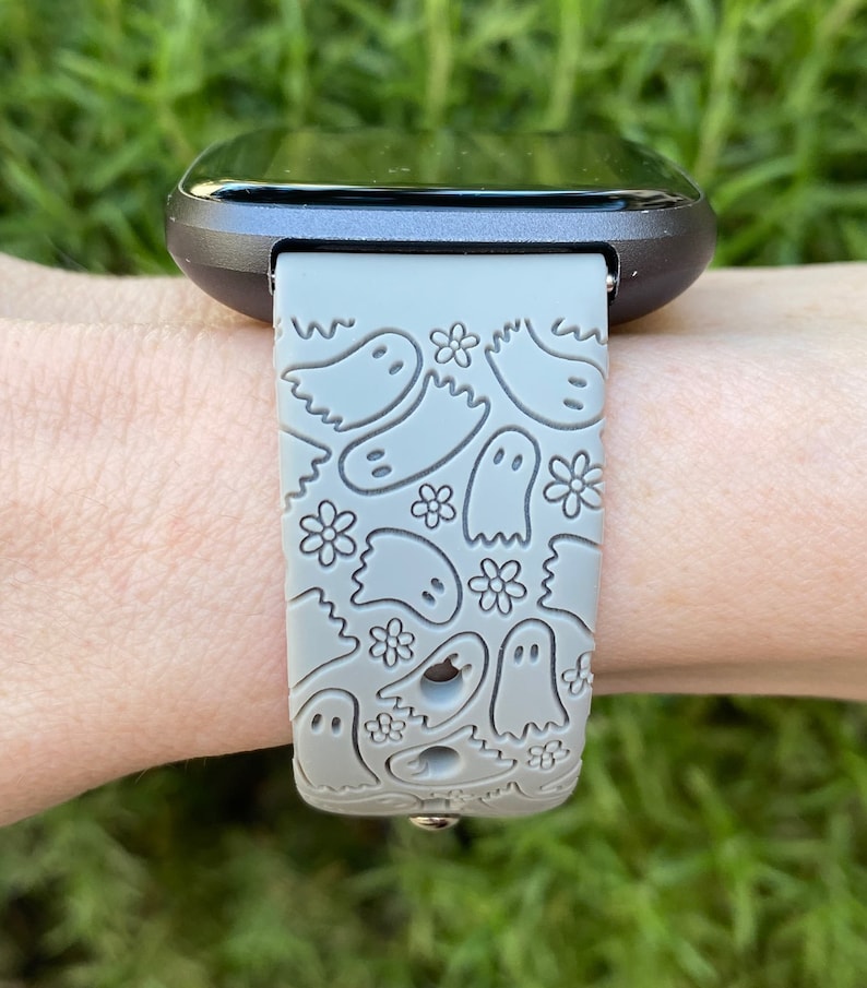 Puede incluir: Una correa de reloj de silicona gris con un patr&oacute;n de fantasmas. La correa est&aacute; dise&ntilde;ada para un reloj inteligente con una esfera negra.