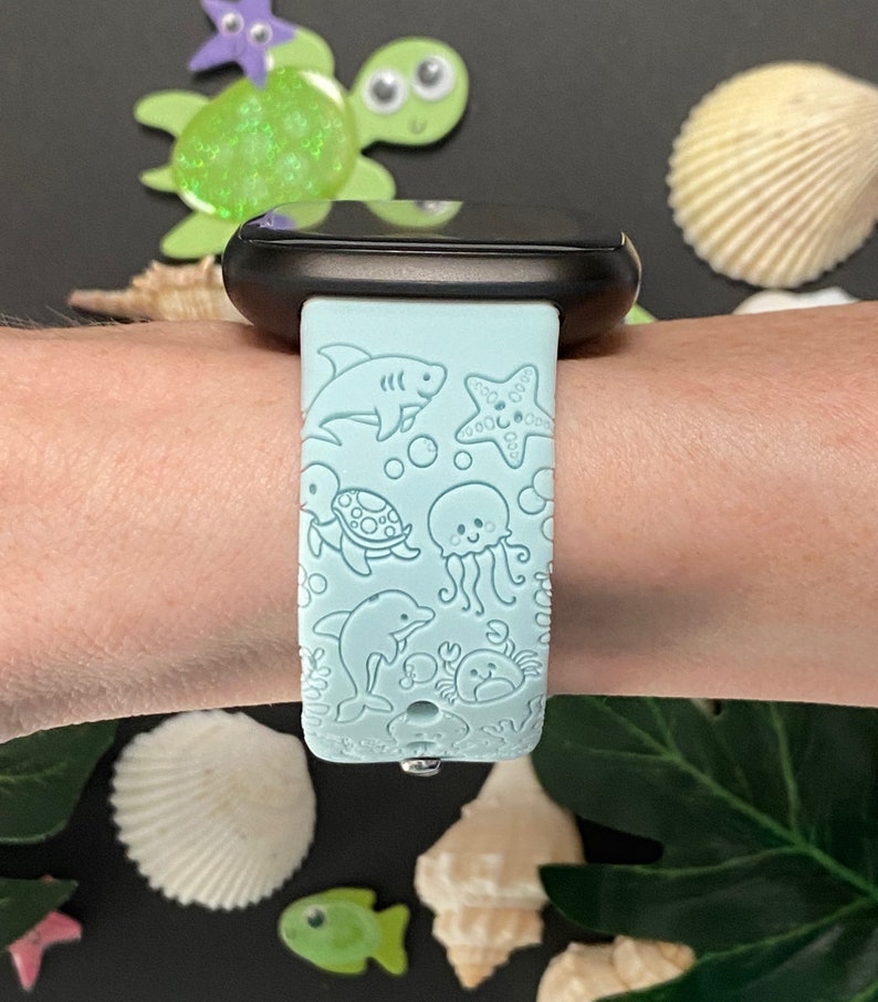 May include: A light blue silicone watch band with a sea-themed design. The band features a shark, starfish, turtle, jellyfish, dolphin, and crab.