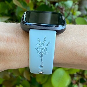 以下が含まれることがあります： 花柄のライトブルーシリコン製腕時計バンド。バンドは、黒い文字盤のスマートウォッチ用に設計されています。