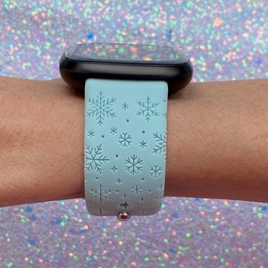May include: A light blue smartwatch band with a snowflake pattern. The band is made of silicone and has a silver buckle.