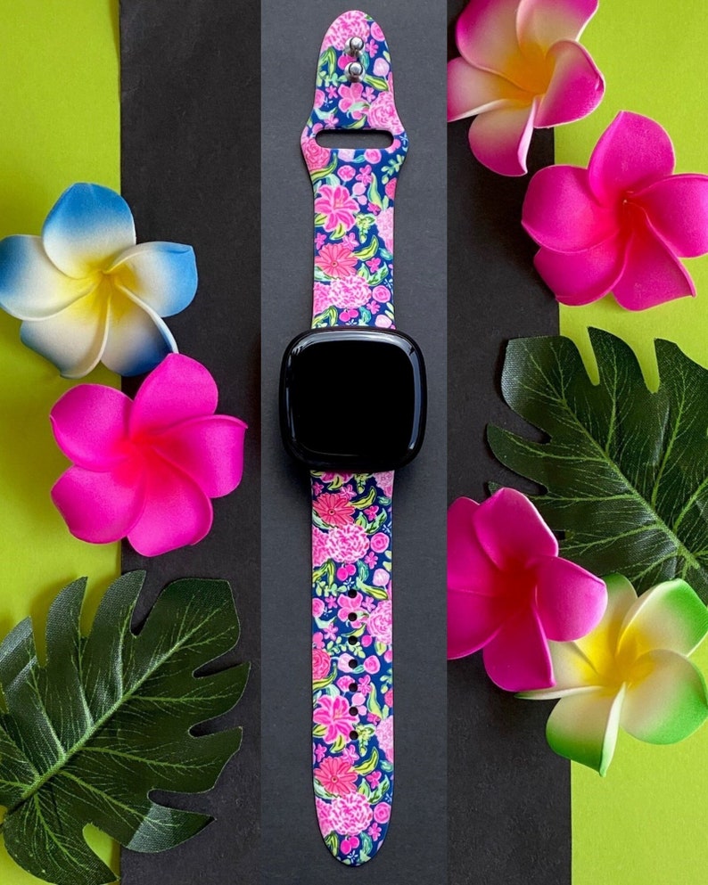 Pu&ograve; includere: Un cinturino per orologio floreale rosa e blu per uno smartwatch. Il cinturino &egrave; in silicone e presenta una stampa floreale. Il cinturino dell'orologio &egrave; mostrato su uno sfondo nero con fiori rosa.