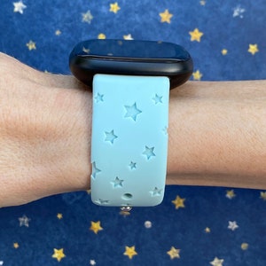 May include: A light blue silicone watch band with a star pattern. The band is designed for a smartwatch and has a silver metal clasp.