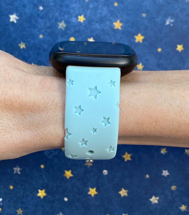 May include: A light blue silicone watch band with a star pattern. The band is designed for a smartwatch and has a silver metal clasp.