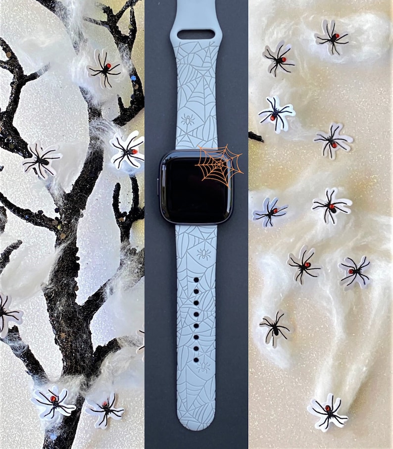 May include: A light gray silicone watch band with a spiderweb pattern. The band is shown on a watch with a black face. The background is a white surface with black spider stickers.