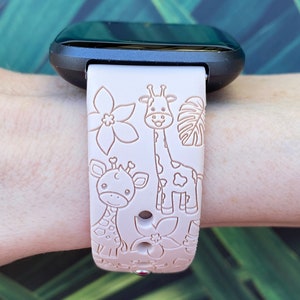 May include: A pink silicone watch band with a giraffe and flower design. The band is compatible with a Fitbit watch.